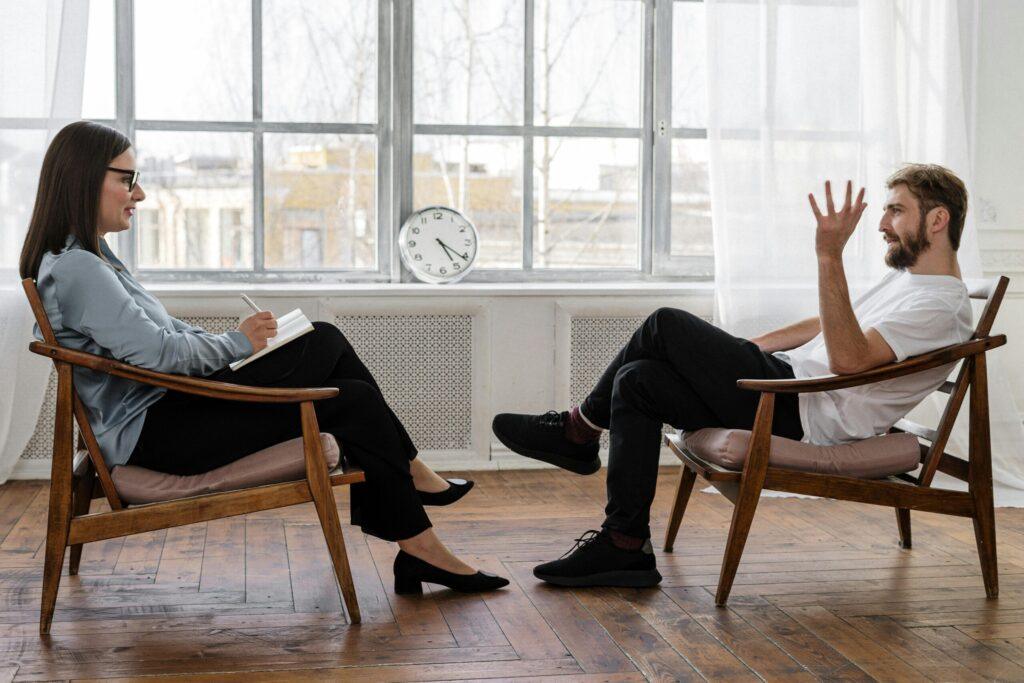 Person in Black Pants and Black Shoes Sitting on Brown Wooden Chair scaled
