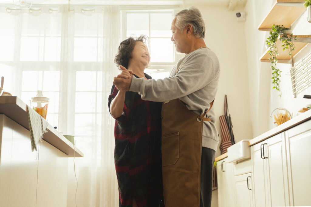Asian senior adult couple cooking healthy food together at home while dancing in the kitchen morning weekend,happiness asian old marry couple enjoy romantic Cropped shot of a senior couple dancing