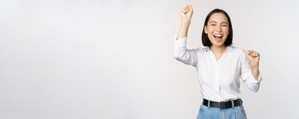 image happy lucky asian woman hooray gesture winning celebrating triumphing raising hadns up laughing standing white background