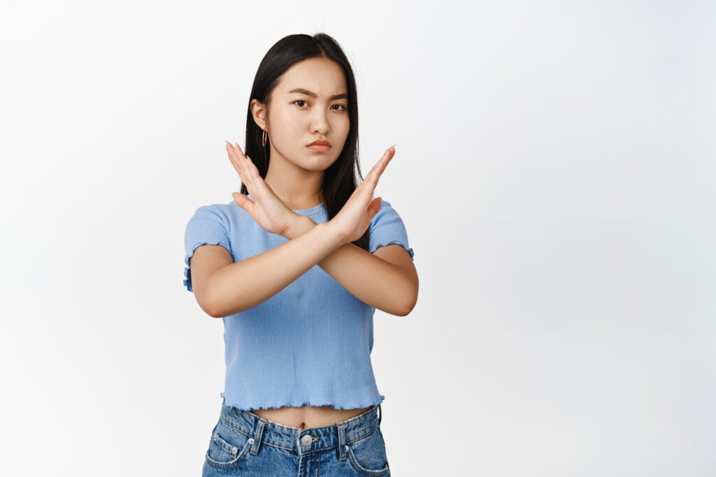 young asian woman shows cross stop block gesture tell no prohibit something bad frowning displeased standing white background